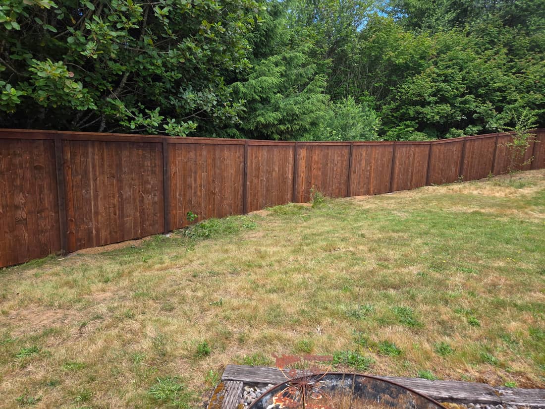 Long cedar privacy fence with a dark brown finish around a lawn in the Portland, OR area