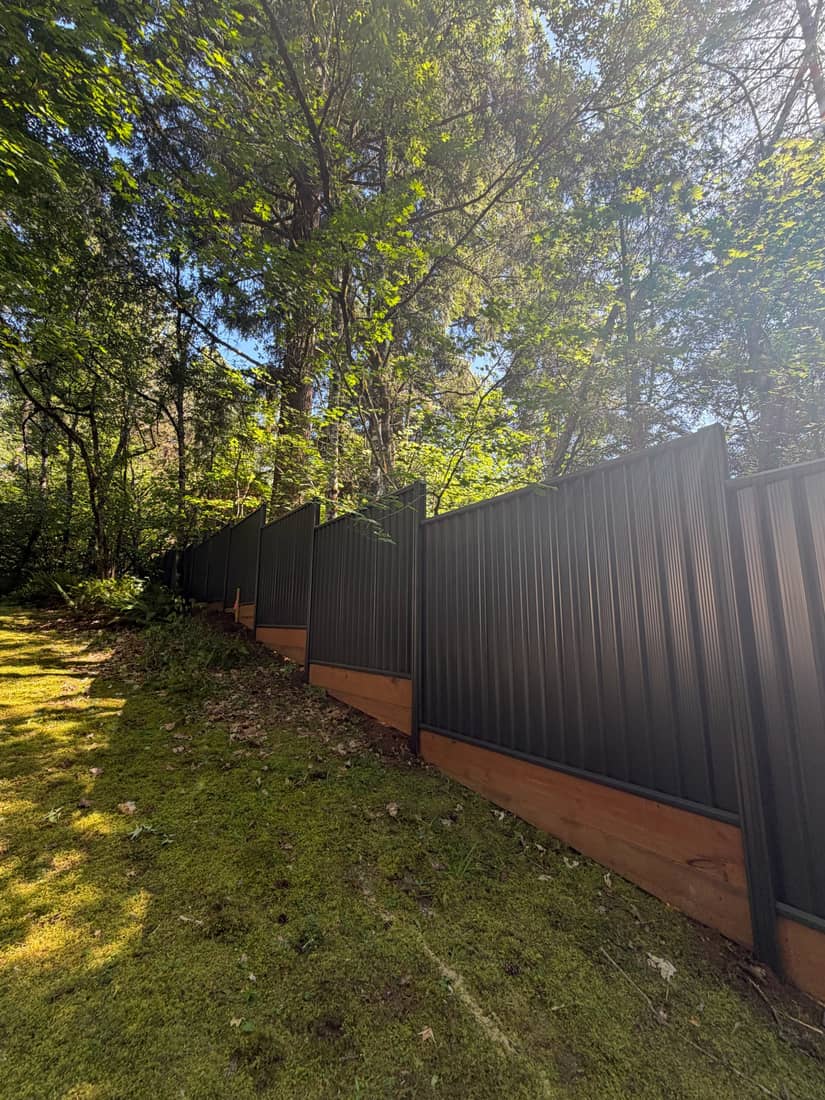 Long run of dark steel privacy fence on a cedar kickboard following the grade of a side yard, Portland OR