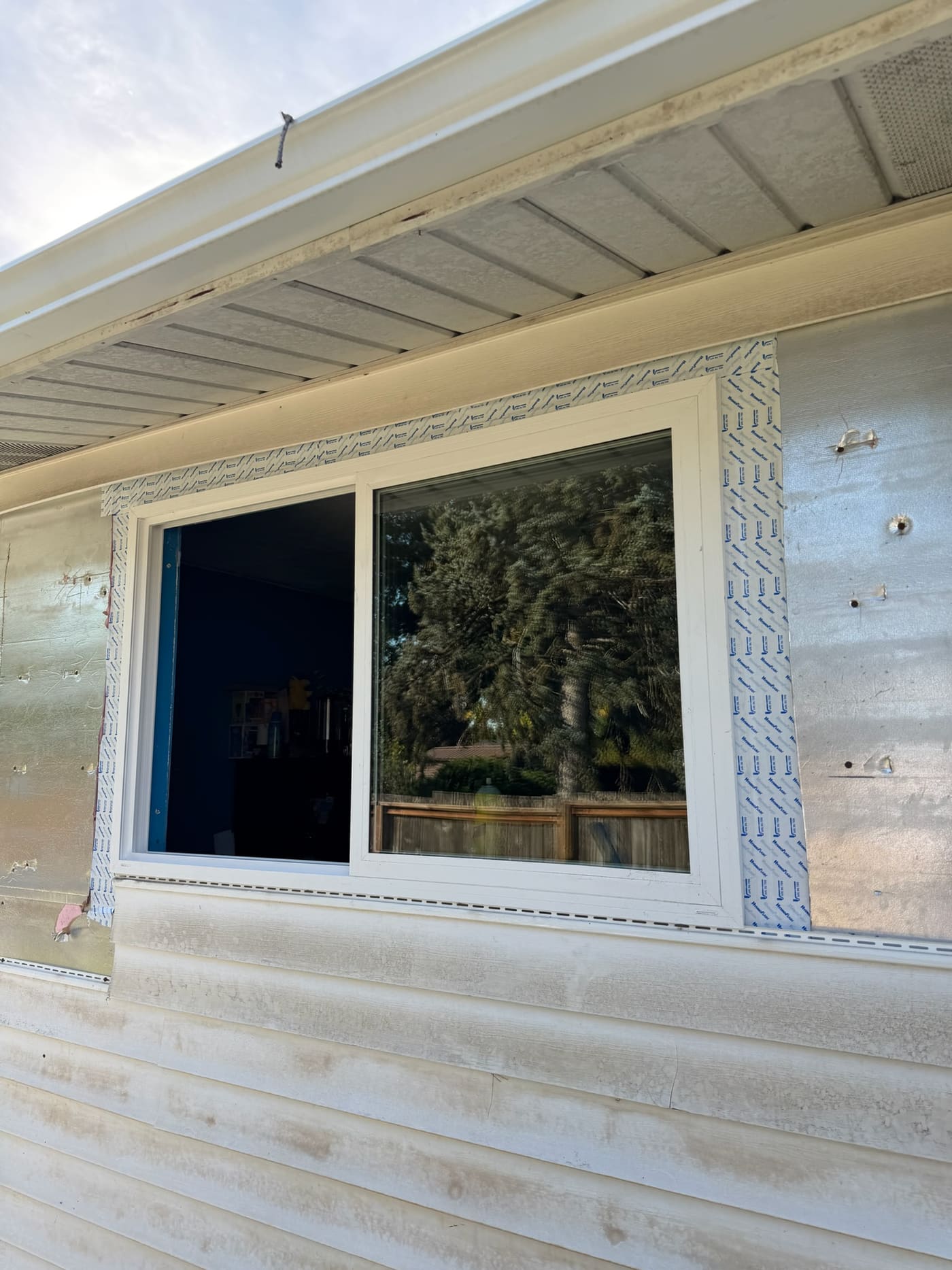 A new white vinyl slider window set in the opening with flashing tape around the frame, before the siding goes back on